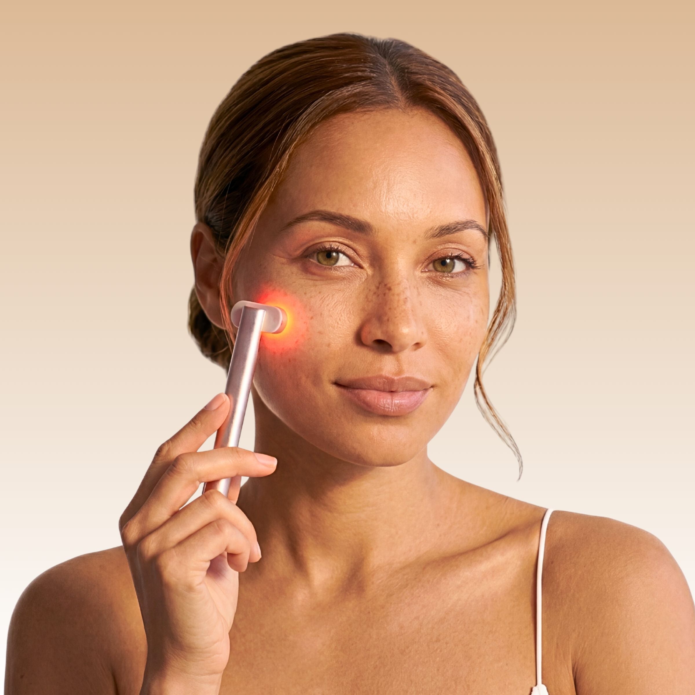 Femme utilisant le Soin LED Précision Auréa™ rose gold, lumière rouge allumée sur la joue